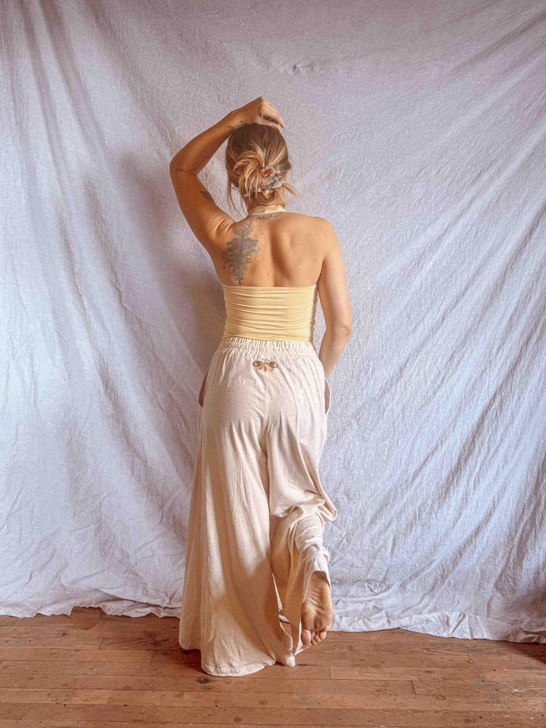 K&ouml;nnte beinhalten: Ein blassgelbes, tr&auml;gerloses Schlauchoberteil kombiniert mit einer locker sitzenden, cremefarbenen Hose mit weitem Bein. Die Hose verf&uuml;gt &uuml;ber einen elastischen Bund mit einem kleinen, gestickten Mottenmotiv mittig unter dem Bund.