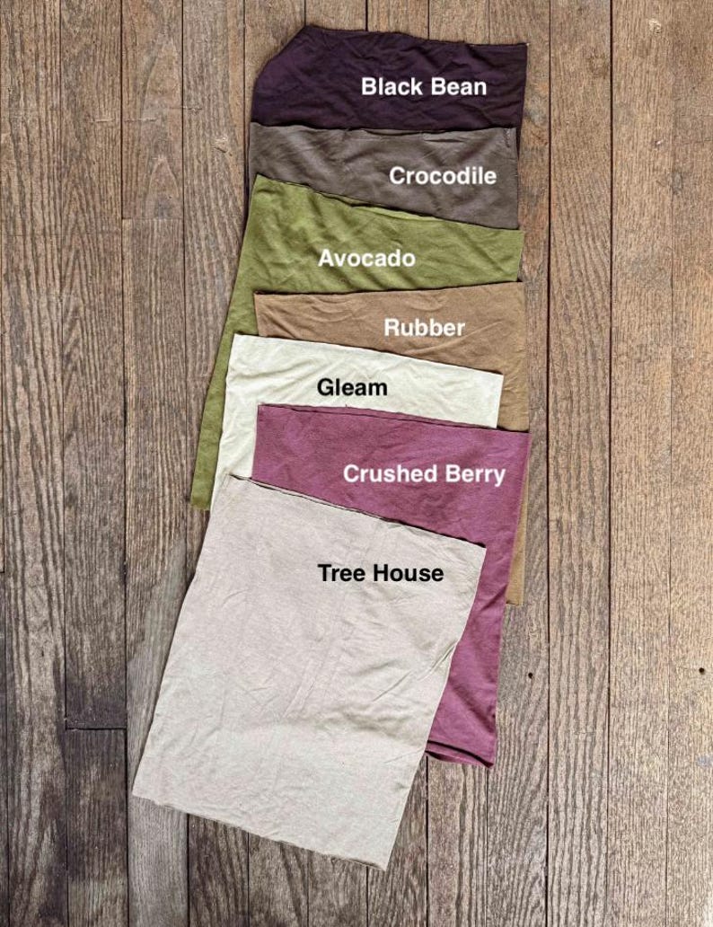May include: A collection of fabric swatches in various colors, including Black Bean, Crocodile, Avocado, Rubber, Gleam, Crushed Berry, and Tree House. Each swatch has a label with its corresponding color name. The swatches are arranged on a wooden surface.