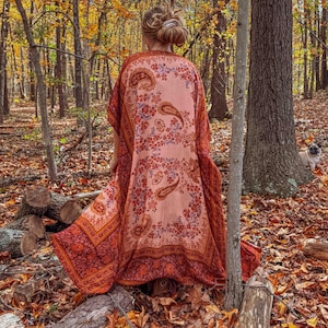 Może przedstawiać: Długie, zwiewne kimono z wzorem paisley w odcieniach brzoskwini, pomarańczy i bordowym. Kimono jest noszone na zewnątrz w leśnym otoczeniu z jesiennymi liśćmi i drzewami.