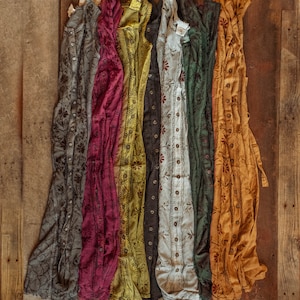 May include: Seven different patterned cotton dresses in various colors, including gray, burgundy, yellow, green, white, and orange, hanging on a wooden surface.