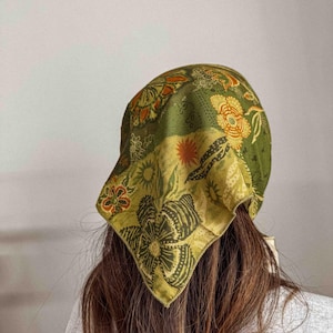 Puede incluir: Un pa&ntilde;uelo verde con un estampado floral en tonos naranja, amarillo y verde. El pa&ntilde;uelo, de forma cuadrada, se lleva en la cabeza. La tela parece suave y ligera.