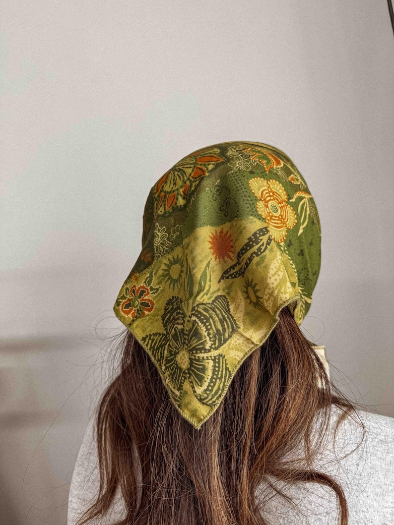 Puede incluir: Un pa&ntilde;uelo verde con un estampado floral en tonos naranja, amarillo y verde. El pa&ntilde;uelo, de forma cuadrada, se lleva en la cabeza. La tela parece suave y ligera.