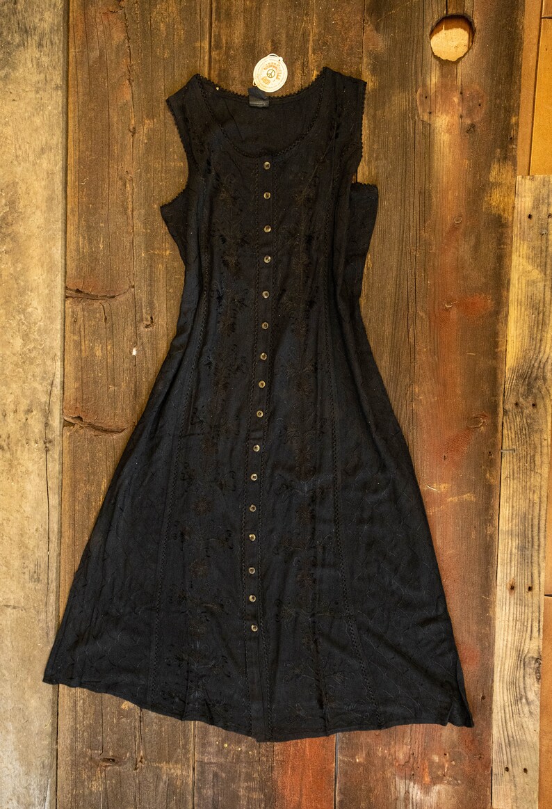 May include: A black sleeveless maxi dress with a button-up front and delicate embroidery. The dress has a flowy silhouette and a relaxed fit.