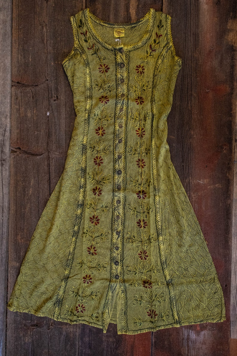 May include: Olive green sleeveless dress with floral embroidery. The dress features a button-down front, intricate stitching, and a flowing A-line skirt. The embroidery includes maroon and yellow floral patterns.