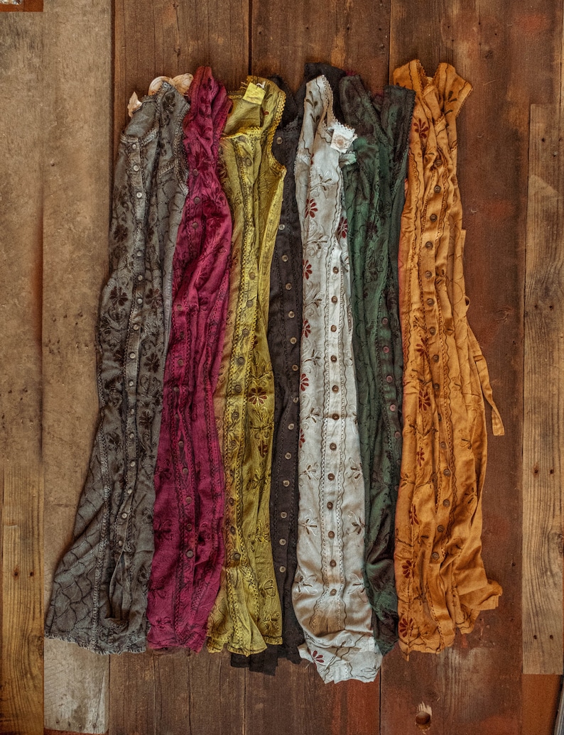 May include: Seven different patterned cotton dresses in various colors, including gray, burgundy, yellow, green, white, and orange, hanging on a wooden surface.
