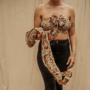 May include: A brown and blue floral print top with a large bow in the front. The top is tied at the waist and is worn with black pants.