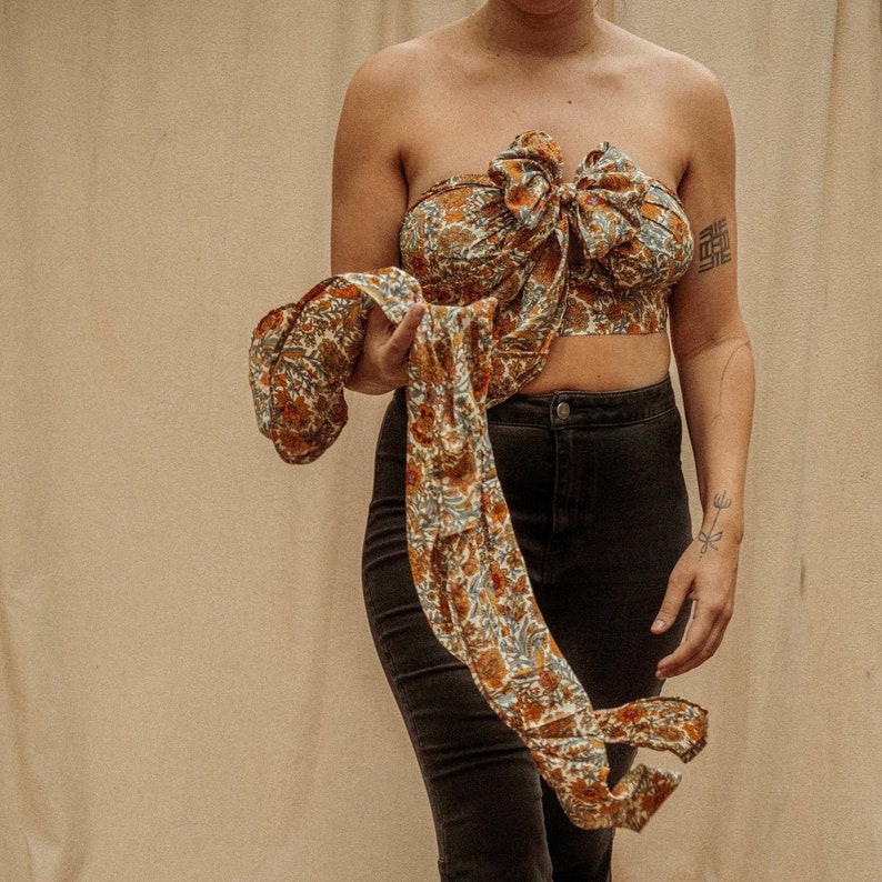 May include: A brown and blue floral print top with a large bow in the front. The top is tied at the waist and is worn with black pants.