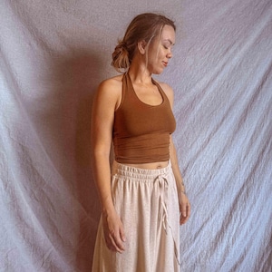 K&ouml;nnte beinhalten: Ein einfarbig braunes, &auml;rmelloses Neckholder-Top mit rundem Ausschnitt, kombiniert mit einem hellbeigen Rock mit hoher Taille, elastischem Bund und einem funktionalen Kordelzug auf der Vorderseite, das ein schlichtes zweiteiliges Outfit bildet.