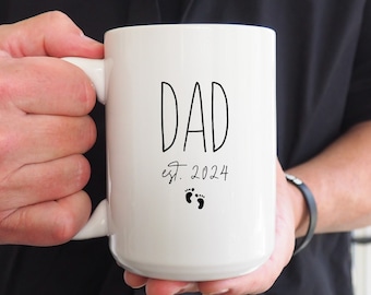 May include: White ceramic mug with black text that reads "DAD est. 2024" with two small black footprints below the text.