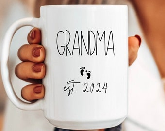 May include: White ceramic mug with black text that reads "Grandma est. 2024" and a small footprint graphic.