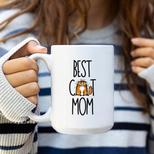 May include: White ceramic mug with a black and white graphic of a cat and the text "Best Cat Mom".