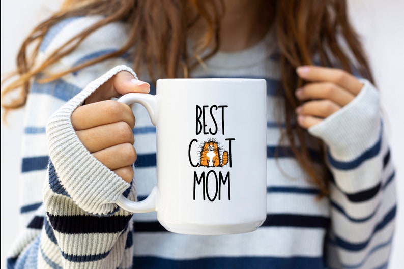 May include: White ceramic mug with a black and white graphic of a cat and the text "Best Cat Mom".