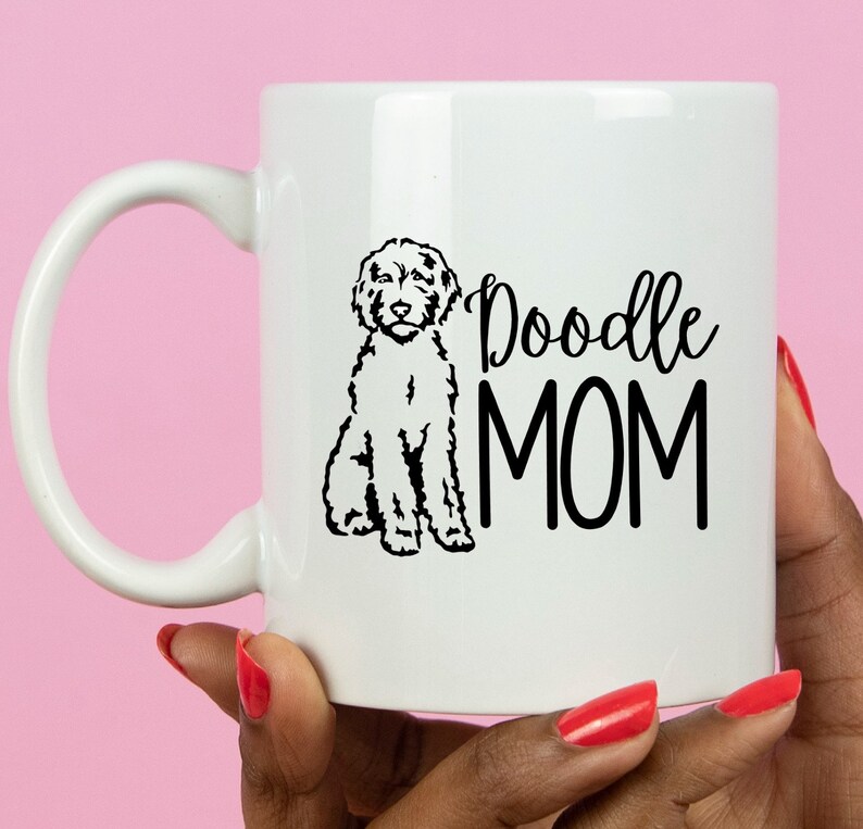 Op de afbeelding: Witte keramische koffiemok met een zwart silhouet van een poedel en de tekst "Doodle MOM" in zwart.