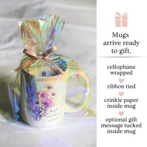 Op de afbeelding: Een witte keramische mok met een bloemenpatroon en de tekst "best auntie ever". De mok is verpakt in cellofaan en vastgebonden met een lint. Hij is klaar om als cadeau te worden gegeven.