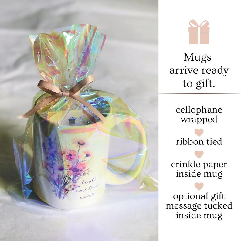 Op de afbeelding: Een witte keramische mok met een bloemenpatroon en de tekst "best auntie ever". De mok is verpakt in cellofaan en vastgebonden met een lint. Hij is klaar om als cadeau te worden gegeven.