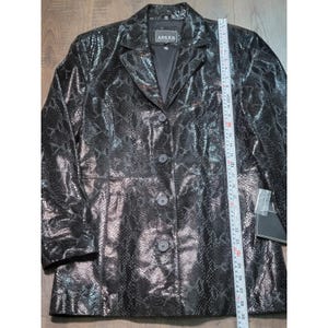 May include: A black blazer with a snakeskin pattern, featuring a notched collar, four front buttons, and a label reading Adler Collection. A white measuring tape is placed vertically along the front, showing a length of approximately 29 inches.