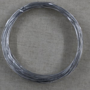 May include: A coil of silver-colored wire, wound into a circle, on a light brown fabric background.