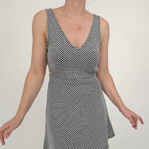 May include: A sleeveless black and white polka dot dress with a V-neckline and a cut-out detail at the waist. The dress has a flared skirt and is knee-length. The fabric has a repeating pattern of small white dots on a black background.