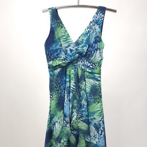 Könnte beinhalten: Ärmelloses V-Ausschnitt-Kleid mit blauem und grünem Schmetterlingsflügelmuster. Das Kleid hängt an einem silbernen Kleiderbügel. Der Stoff ist leicht und hat ein fließendes Design mit geraffter Taille und Rüschensaum.