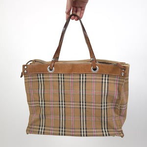 Peut inclure: Un sac cabas en toile à carreaux marrons et beiges avec des anses et des accents en cuir. Le sac a des œillets métalliques et une fermeture à glissière.
