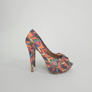 Op de afbeelding: Een enkele platformpumps met hoge hakken en een kleurrijk geometrisch patroon. De schoen heeft een peep-toe ontwerp en een hoge stilettohak. Het patroon bevat tinten oranje, blauw, geel en bruin.