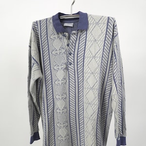 May include: A long-sleeved polo shirt with a geometric pattern in shades of gray and blue. The shirt features a collared neckline and button-up placket. The cuffs and collar are a solid blue color.