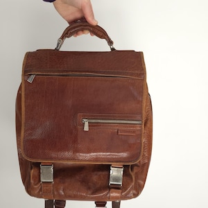 May include: A brown leather backpack with silver buckles and a zipped pocket on the front.