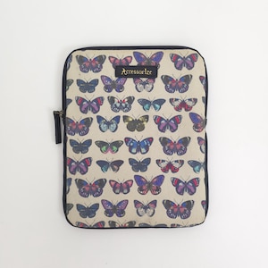 May include: A beige tablet sleeve with a repeating pattern of colorful butterflies. The sleeve has a black zipper and trim. The word "Accessorize" is printed on the front.