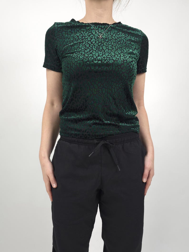 May include: A dark green velvet top with a black leopard print pattern. The top has short sleeves and a gathered waist. Paired with black drawstring pants. A silver necklace is visible.