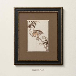 May include: A framed wall art piece featuring a detailed line drawing of a bird perched on a flowering branch. The artwork is set against a cream background within a brown mat, all enclosed in a black frame with gold-toned inner detailing.