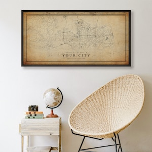 May include: A vintage-style map print in a brown frame, featuring a detailed map of a city with roads and streets. The map is printed on a beige background with a brown border. The text "YOUR CITY" is printed below the map, along with coordinates and the state or country.
