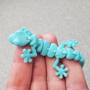 May include: A light blue articulated lizard toy. The toy is made of plastic and has a segmented body, with jointed legs and a head. The lizard is designed to be flexible and poseable. The toy is a fun and engaging item for children.