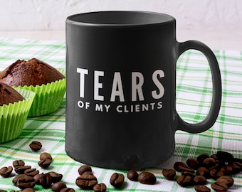 May include: Black coffee mug with white text that reads "Tears of my clients". The mug is sitting on a green and white checkered tablecloth with coffee beans and chocolate muffins.