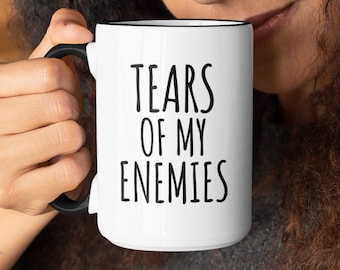 May include: A white ceramic mug with a black rim and handle. The mug has black text that reads "Tears of my Enemies".