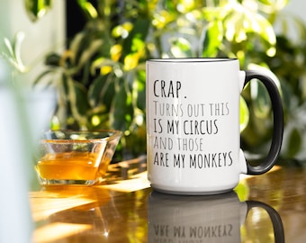 May include: A white ceramic mug with a black handle and rim, featuring the black printed text: CRAP. Turns out this is my circus and those are my monkeys. The mug has a cylindrical body and a smooth finish, standing upright on a reflective surface.