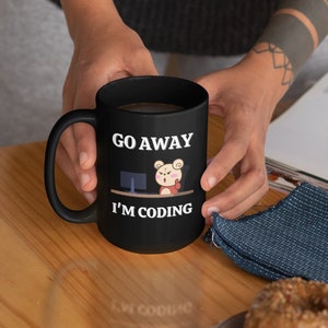 May include: A black coffee mug with a white design that says "Go Away I'm Coding" and a cartoon bear sitting at a computer.