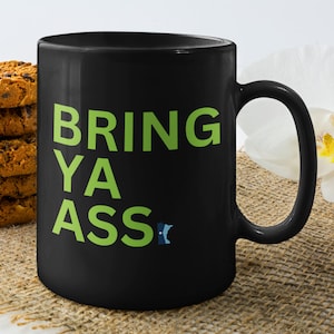 May include: Black ceramic coffee mug with a green graphic that says "BRING YA ASS".
