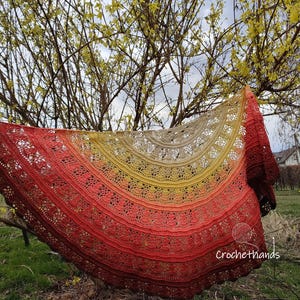 May include: A crocheted shawl with a gradient of colours from beige to yellow to orange to red. The shawl is draped over a branch of a tree with yellow blossoms. The text "Crochethands" is visible in the lower right corner of the image.