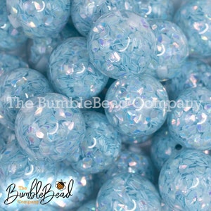May include: A close-up of a group of light blue bubblegum beads with iridescent glitter inside. The beads are scattered in a pile.