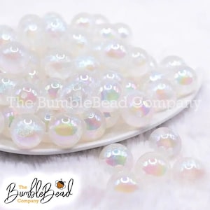 May include: A close-up of a pile of iridescent white glass beads. The beads are round and have a slight shimmer to them. The beads are arranged in a pile on a white surface.