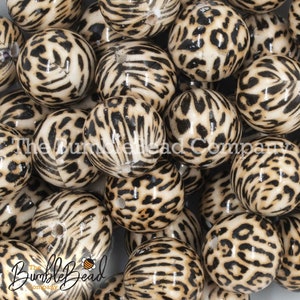May include: A close-up of a pile of round, white beads with a black and brown leopard print pattern.