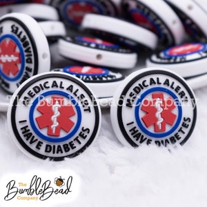 May include: A close-up of two white silicone medical alert beads with black trim. The beads have a red and blue medical symbol with the text "MEDICAL ALERT I HAVE DIABETES".