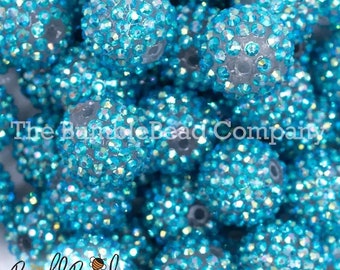 May include: Close-up of a pile of turquoise blue round beads covered in iridescent rhinestones. The beads are all the same size and are arranged in a random pattern.