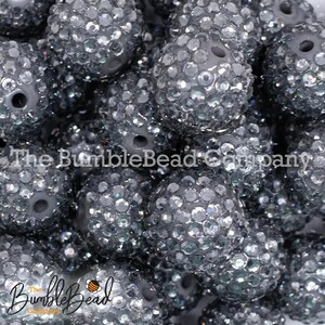 May include: A close-up of a pile of silver glitter-covered round beads. The beads are all the same size and have a hole in the center. The beads are arranged in a random pattern.