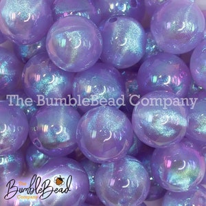 May include: A collection of iridescent purple beads. The beads are round and have a shiny, reflective surface. The text "The BumbleBead Company" is visible on the beads.