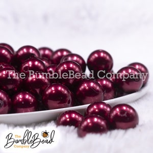 May include: A bowl filled with burgundy pearl beads. The beads are round and have a high gloss finish.