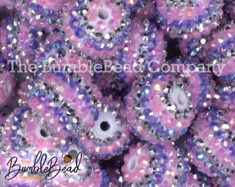 May include: A close-up of a pile of pink and purple round beads with silver glitter and iridescent accents. The beads have a white center with a hole for stringing.