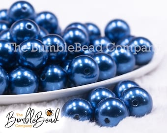 May include: A close-up of a white bowl filled with blue pearl beads. The beads are round and have a metallic sheen. The bowl is sitting on a white fuzzy surface.
