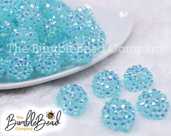 May include: A pile of light blue iridescent round bubble beads with a white background. The beads are about 1 inch in diameter and have a sparkly finish.