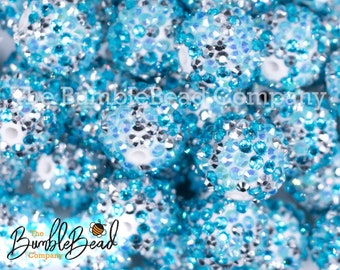 May include: Close-up of a group of white and blue round beads covered in small, sparkly rhinestones. The beads are arranged in a random pattern, creating a shimmering and colorful display.